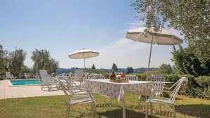 Un espace piscine extérieur doté de chaises longues et de parasols, entouré de verdure et avec des collines en arrière-plan.