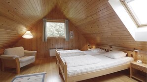 Een gezellig slaapkamer op zolder met houten wanden en een schuine kap, met twee bedden, een stoel en een kleine tafel.