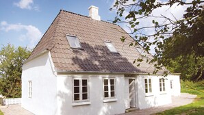 Ett vitt hus med ett tak täckt av takpannor, två fönster och en liten veranda.