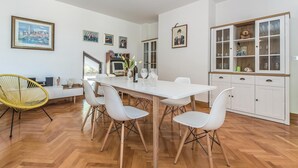 Ein moderner Essbereich mit einem weißen Tisch, vier weißen Stühlen und einem gelben Stuhl. An der Wand befinden sich gerahmte Bilder, ein Schrank mit Glastüren und ein Holzboden.