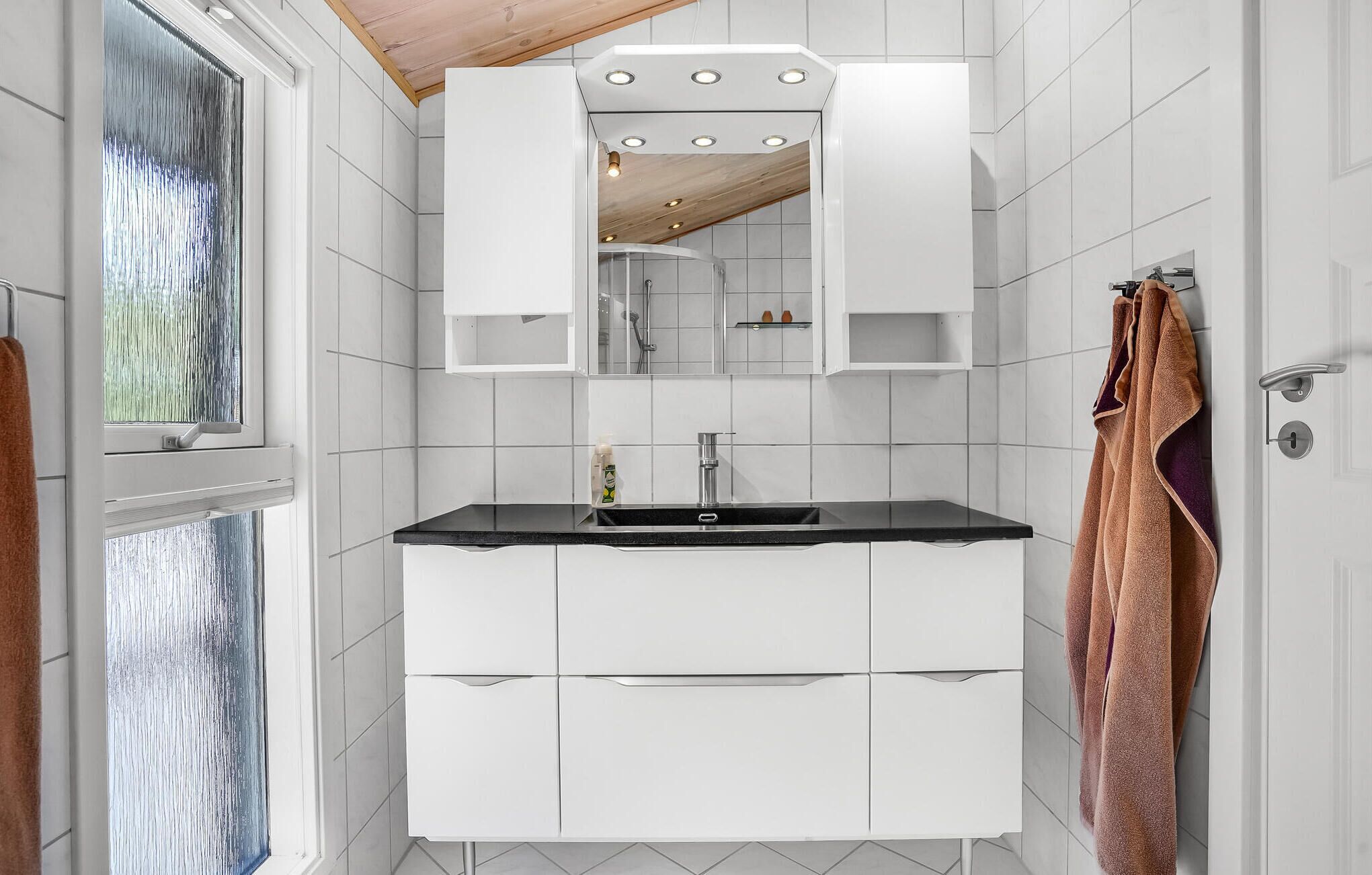 Une salle de bain moderne avec un lavabo sur un plan de travail noir, des meubles blancs et un grand miroir.