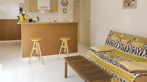 A compact living space with a kitchenette, two wooden stools, a sofa with zebra print, and a wooden coffee table. - Lovely home in Cazevieille with kitchen (Cazevieille)