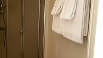 A bathroom with a shower, a towel rack with towels, and a visible door.