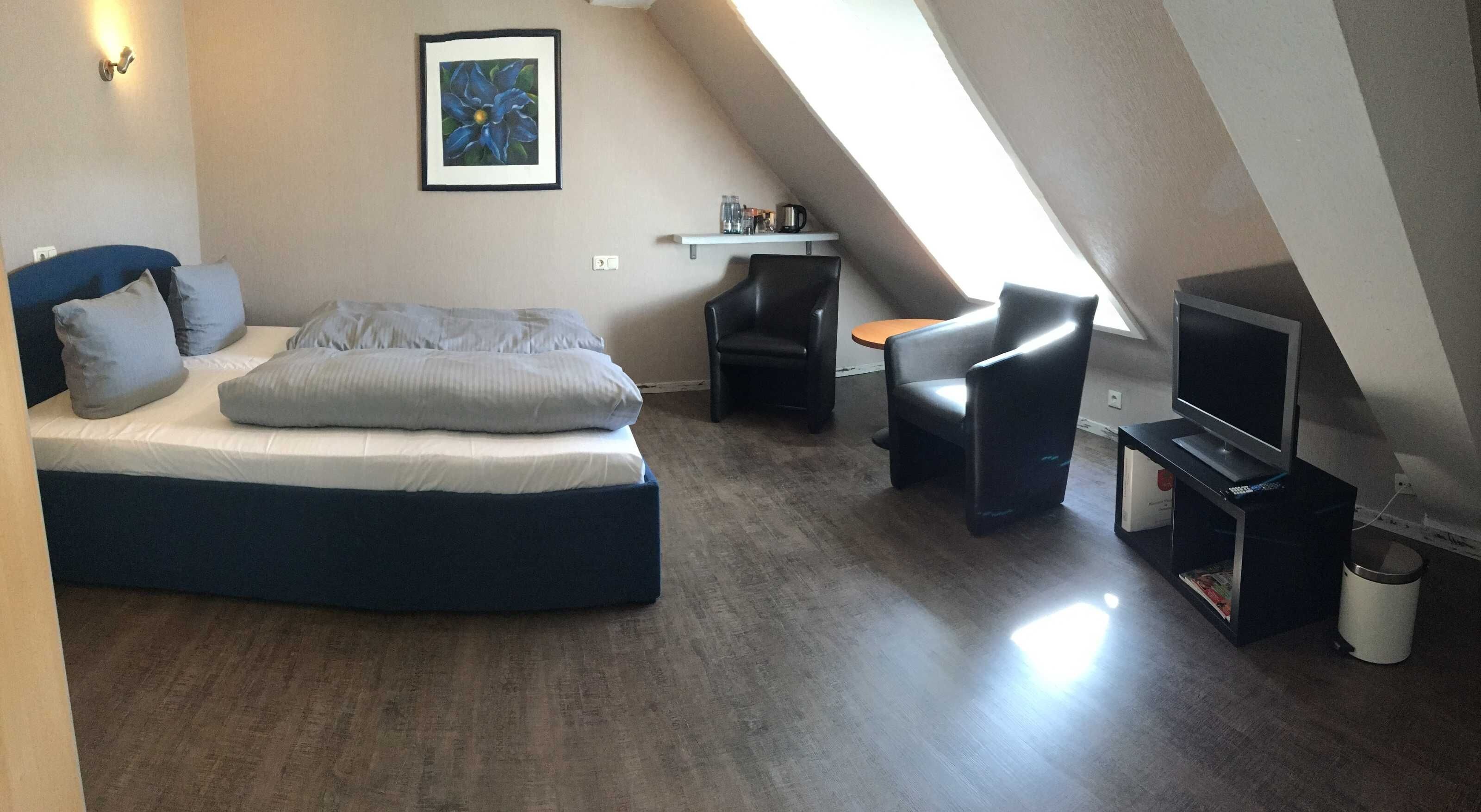 Une chambre à coucher avec un lit, une chaise, une petite table, un téléviseur et un tableau accroché au mur.