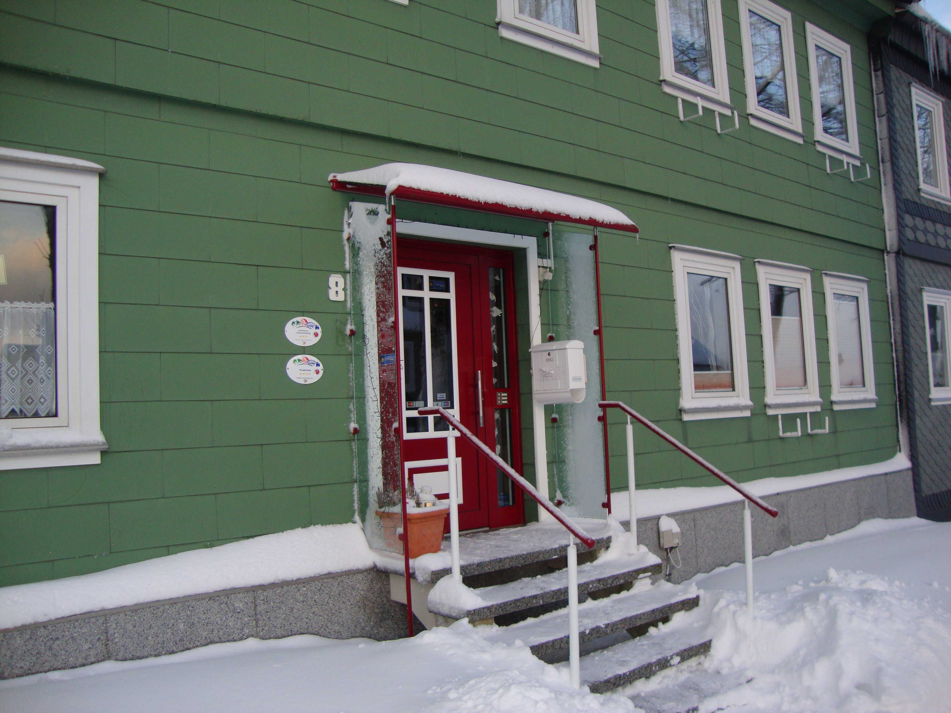 Un edificio verde con puerta roja, ventanas blancas y entrada cubierta de nieve.