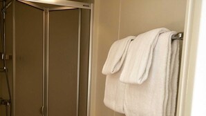Un baño con ducha, un perchero con toallas y una puerta a la vista.