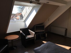 Una habitación con tragaluz, televisión, cama y una pequeña mesa.