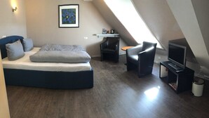 Un dormitorio con una cama, una silla, una mesita, un televisor y un cuadro en la pared.