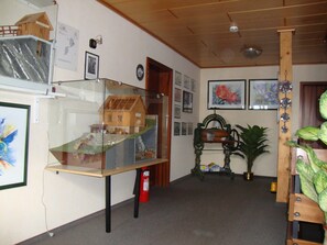 A room with a wooden ceiling, a glass display case with a model house, framed pictures on the wall, and a fire extinguisher on the floor. - Double room no. 9 - Gästehaus Hohensee (Clausthal-Zellerfeld)