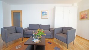 Ein modernes Wohnzimmer mit einer grauen Sofagarnitur, einem Couchtisch mit Blumenvase und einem weißen Kleiderschrank.