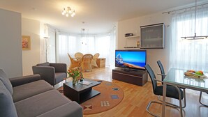 Ein modernes Wohnzimmer mit Fernseher, bequemen Sitzgelegenheiten und einem Essbereich.