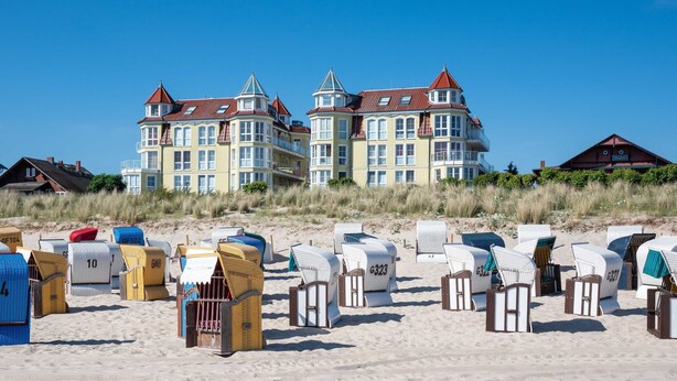 Ein Strandgrundstück mit mehreren Strandkörben und einem großen Gebäude mit zahlreichen Balkonen.