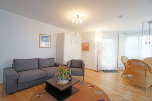 Uma sala de estar moderna com um sofá cinza, uma mesa de centro com flores, um armário, cadeiras de vime e um abajur.