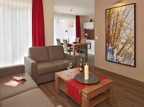 Une chambre d’hôtel moderne avec un canapé, une petite table en bois sur laquelle est posée une bougie, et un tableau accroché au mur.