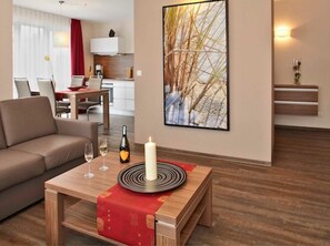 Ein modernes Wohnzimmer mit Sofa, Essbereich, Küche und einem großen gerahmten Bild an der Wand.
