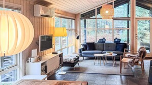 A cozy living room with a large window, a sofa, a coffee table, and a TV. - Beautiful home in ålbæk with sauna (Ålbæk)