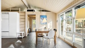 A modern kitchen with a built-in refrigerator, a dining area with a wooden table and chairs, and large windows offering a view of the outdoors. - Beautiful home in ålbæk with sauna (Ålbæk)
