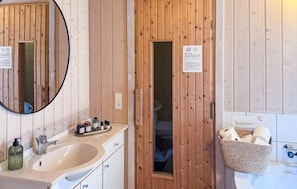 A wooden bathroom with a sink, mirror, and a small window. There are toiletries on the counter and a basket with towels. - Beautiful home in ålbæk with sauna (Ålbæk)