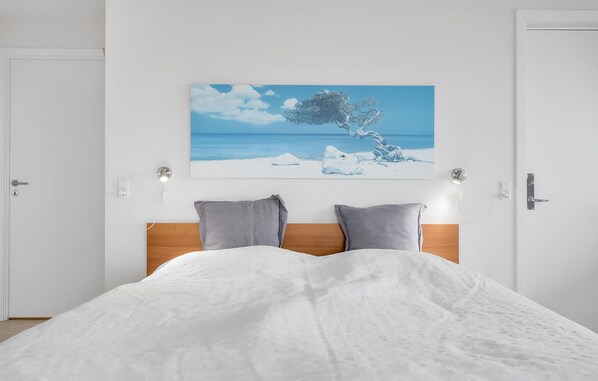 A bedroom with a bed, a painting of a tree and beach, and two bedside lamps. - Lovely apartment in Gudhjem with swimming pool (Gudhjem)
