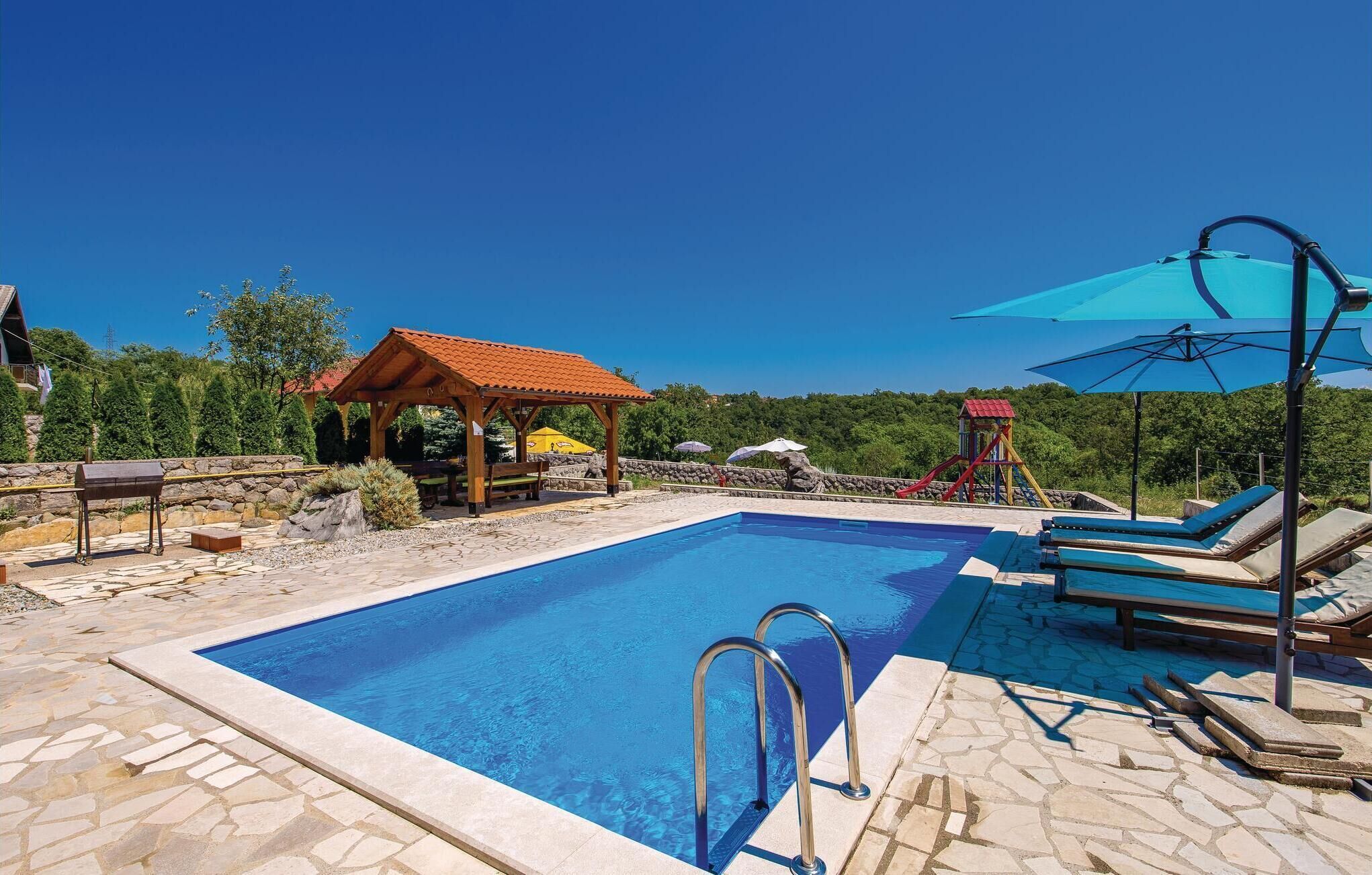 A swimming pool with a wooden gazebo, lounge chairs, and a children's play area.