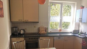 A kitchen with a window, a table with a coffee-themed tablecloth, and various kitchen appliances. - *Windrose 23 measure GM 69552 - Windrose 23 - SNR: 10 (Graal-Müritz)