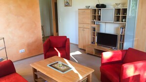 A living room with red sofas, a wooden coffee table, a TV stand, and a bookshelf. - *Windrose 23 measure GM 69552 - Windrose 23 - SNR: 10 (Graal-Müritz)