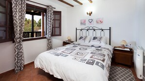 Een slaapkamer met een bed, houten balken, een raam met gordijnen, een nachtkastje, een lamp en een radiator.