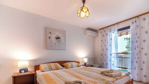 Een slaapkamer met een bed, twee nachtkastjes, een wandairconditioner, een plafondlamp en een raam met gordijnen.