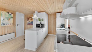 Et moderne køkken med træloft, hvide skabe og en central køkkenø.