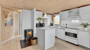 Et moderne køkken med en brændeovn, hvide skabe og en stor køkkenø.