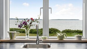 A kitchen with a view of a body of water, a sink, and a vase with flowers on the windowsill.