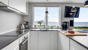 A modern kitchen with a view of the sea, a coffee machine, and a loaf of bread on the counter.