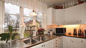 A kitchen with white cabinets, a stainless steel sink, a microwave, and a kettle. There is a window with a view of a house and trees outside. - 4 bedroom stunning home in Färgelanda (Färgelanda)