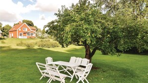 A grassy outdoor area with a white table and chairs, a large tree, and a red house in the background. - 4 bedroom stunning home in Färgelanda (Färgelanda)