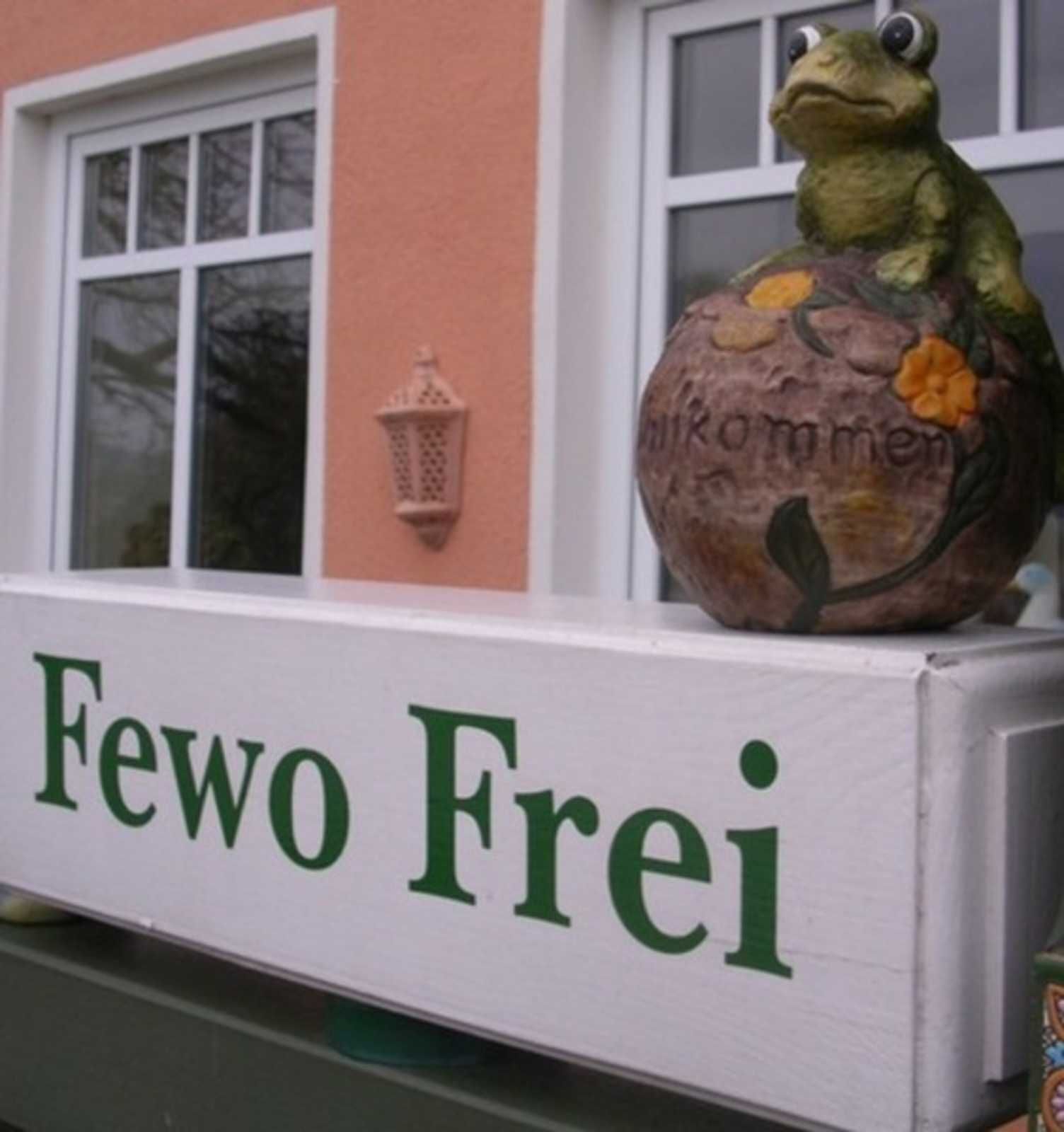 A sign with the text "Fewo Frei" and a frog statue on top.