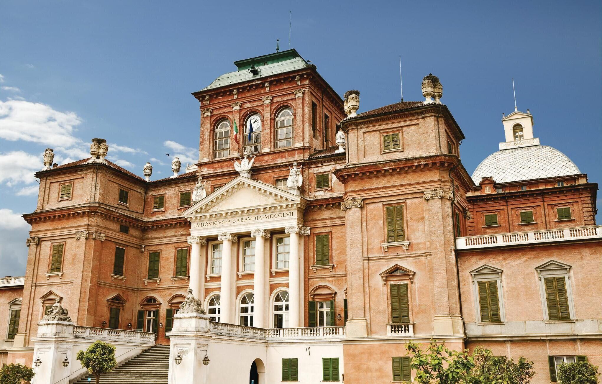 Ein großes, historisches Gebäude mit klassischer Architektur, das einen zentralen Eingang mit Säulen und eine Kuppel auf der rechten Seite zeigt.
