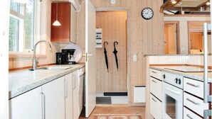 A modern kitchen with wooden walls, a coffee maker, a sink, and two umbrellas hanging on the wall. - Gorgeous home in Væggerløse with WiFi (Væggerløse)