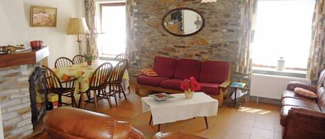 A living room with a stone wall, a red sofa, leather chairs, a dining table with chairs, and a white coffee table.