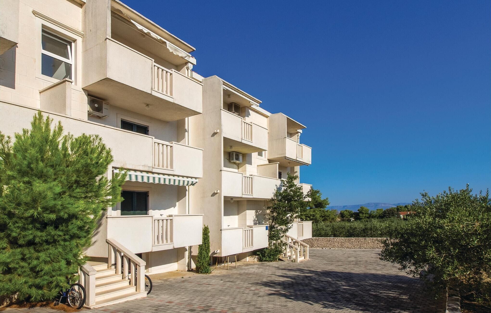 Un edificio residenziale a più piani con balconi, un cortile lastricato e aree verdi circostanti.