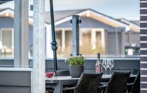 Een terras met een eettafel gedekt voor twee personen, een potplant, een fles wijn en een schaal fruit.