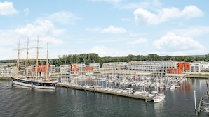 Ein Yachthafen mit mehreren vertäuten Booten, einem großen Schiff auf der linken Seite und modernen Gebäuden im Hintergrund.