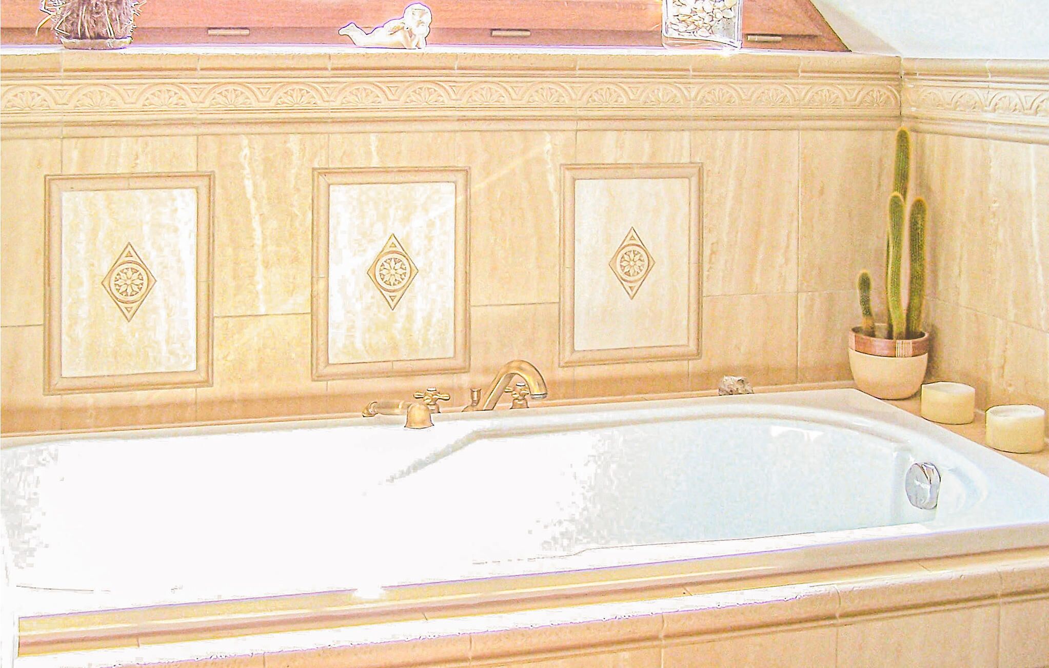 A large bathtub with a single faucet, set against a tiled wall with decorative panels.