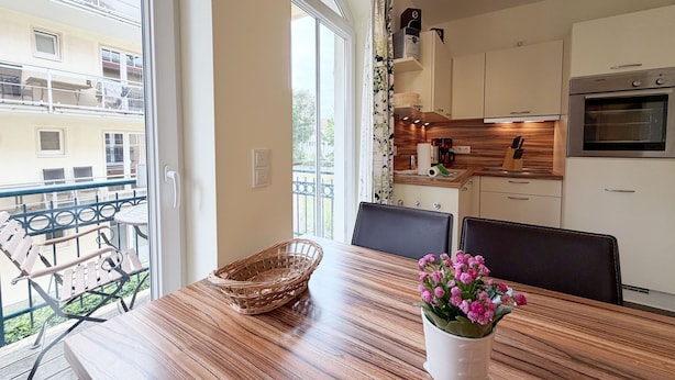 Een moderne keuken met een inbouwoven, een eethoek met een houten tafel en een balkon met zitplaatsen buiten.