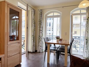 A dining area with a wooden table and chairs, a window with curtains, and a view of the outside balcony.