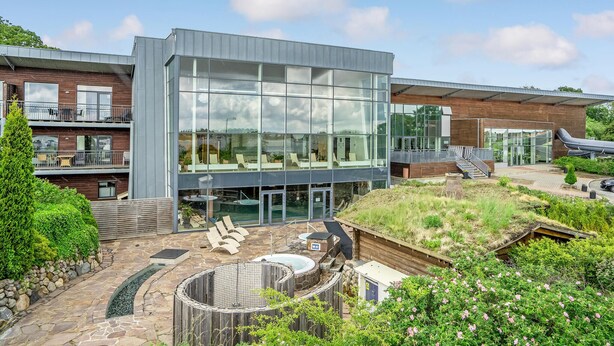 A modern building with large glass windows, a rooftop garden, and a swimming pool.