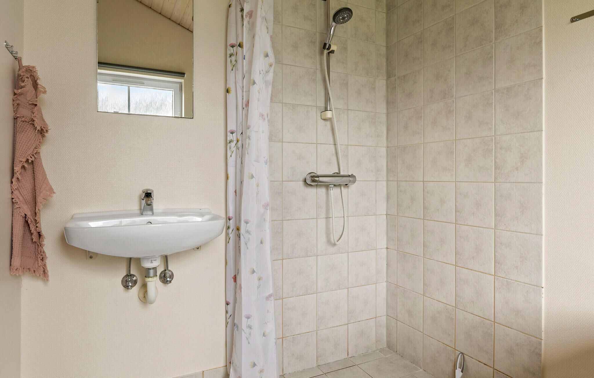 A bathroom with a white sink, a shower with a handheld showerhead, and a window above the sink.
