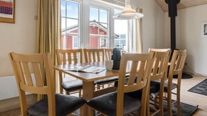 A dining area with a wooden table and chairs, a hanging light fixture, and a view of the outside through large windows.