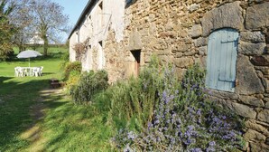 A stone building with a rustic exterior, a small garden with purple flowers, and a white outdoor table and chairs. - Beautiful home in Moelan sur Mer (Moelan sur Mer)