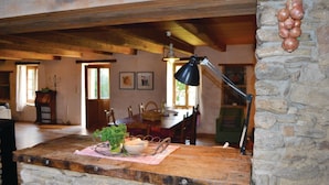 A rustic dining area with a wooden table, a black desk lamp, and a stone wall with onions. - Beautiful home in Moelan sur Mer (Moelan sur Mer)