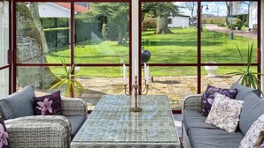 A conservatory with wicker furniture, a glass table, and a view of a well-maintained garden. - Cozy home in Svedala with WiFi (Svedala)